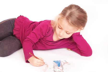 Little cute girl draws pencils lying on the floor on a white backgroundの写真素材