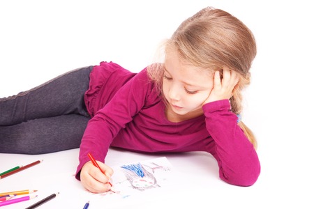 Little cute girl draws pencils lying on the floor on a white backgroundの写真素材