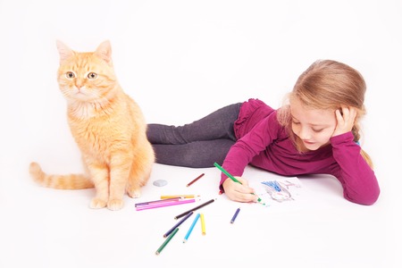 Little cute girl with colored pencils and red cat lying on the floor on a white backgroundの写真素材