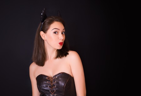 Young cheerful woman in the studio on a black background with bright makeup and horns on her headの写真素材