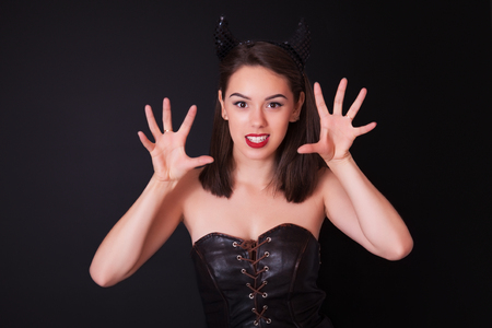 Young cheerful woman in the studio on a black background with bright makeup and horns on her headの写真素材