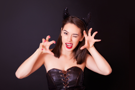Young cheerful woman in the studio on a black background with bright makeup and horns on her headの写真素材