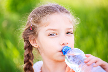 Little cute girl on the nature drinks water from a plastic bottleの写真素材