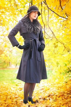 Portrait of a beautiful young woman in a black coat and hat on a background of yellow autumn landscapeの写真素材