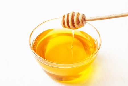Dipper for honey and honey in a bowl on a white backgroundの写真素材