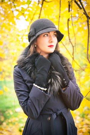 Portrait of a beautiful young woman in a black coat and hat on a background of yellow autumn landscapeの写真素材