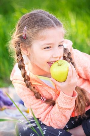 Little cute girl in the garden on a background of green grass with an apple in her handの写真素材