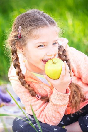 Little cute girl in the garden on a background of green grass with an apple in her handの写真素材