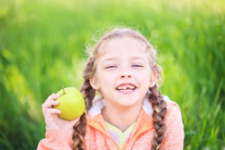 Sweet girl with a fallen tooth holding an apple in her hand on natureの写真素材