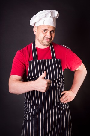 Portrait of a cook man doing a success symbol against a black backgroundの写真素材