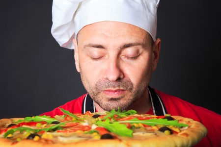 Portrait of happy attractive cook with a pizza in studio an a black backgroundの写真素材