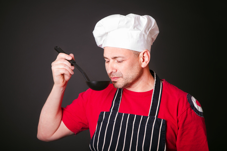 Portrait of a funny cook with a ladle in his hand in the studio on a black backgroundの写真素材