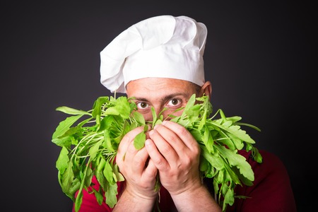 Closeup of happy chef holding arugula beam on black backgroundの写真素材