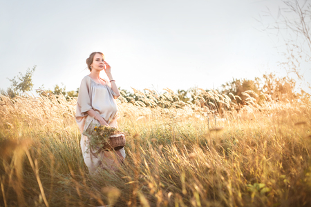 Young beautiful pregnant woman on a walk with wild flowers in her handsの写真素材