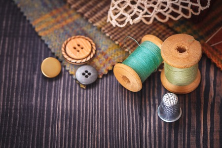 Thimble, buttons, spools of thread and fabric swatches on a wooden background close upの写真素材