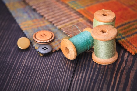 Thimble, buttons, spools of thread and fabric swatches on a wooden background close upの写真素材
