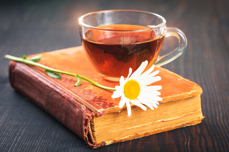 Cup of tea, chamomile and a book on the wooden tableの写真素材
