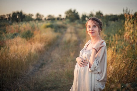 Portrait of a pregnant woman in the sunset light on the nature of the fieldの写真素材