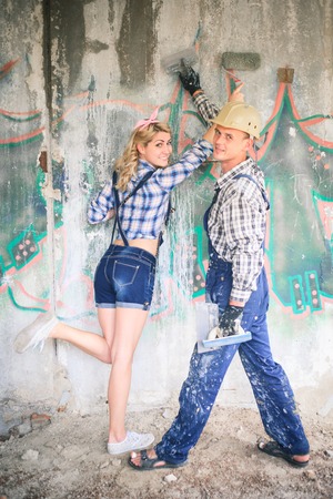 Portrait of a young man and woman in overalls with tools for the repair of the interior in hands. Concept of construction and home repair.の写真素材