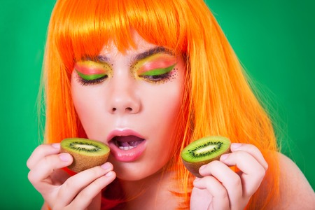 Portrait of red-haired woman in the studio close-up with kiwi.の写真素材