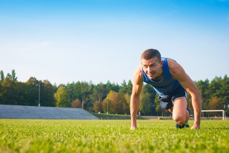 Man in low start position on old stadium. Athlete in starting position. Running, jogging, cardio, sport, active lifestyle concept.の写真素材