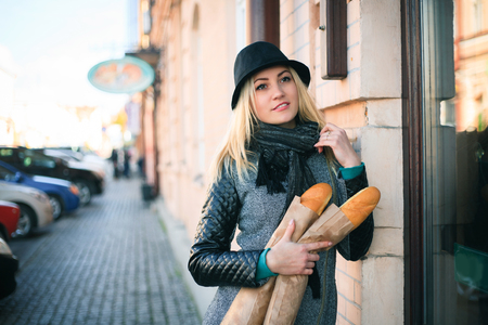 Young beautiful woman with a loaf of bread in her hands in autumn. Outdoors portrait on the street.の写真素材