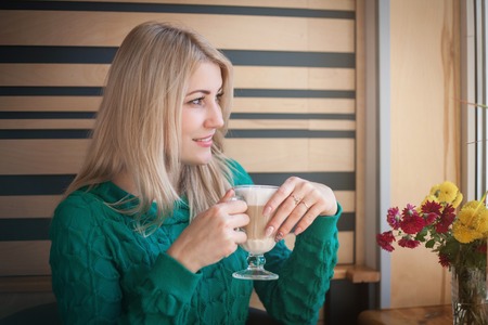 Close-up portrait of a beautiful woman with a cup of coffee at a cafeの写真素材