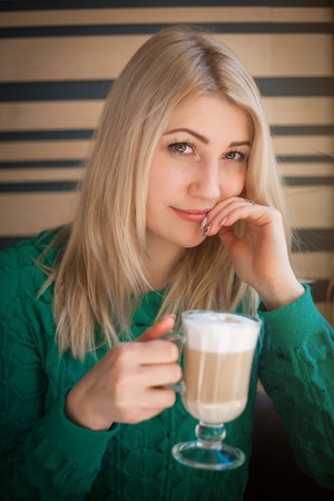 Close-up portrait of a beautiful woman with a cup of coffee at a cafeの写真素材