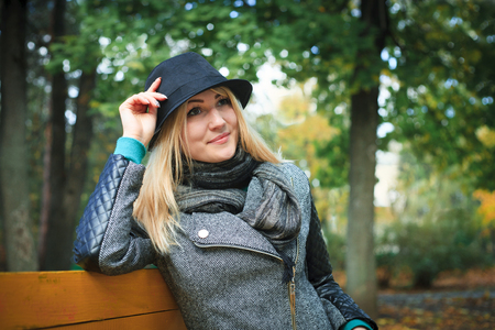 Gorgeous stylish young woman wearing fashionable clothes. Portrait of girl in black hat sitting on bench in park.の写真素材