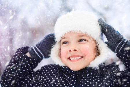Portrait of a cute little girl in a snowy park during a snowfall.の写真素材