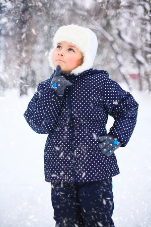 Portrait of a cute little girl in a snowy park during a snowfall.の写真素材