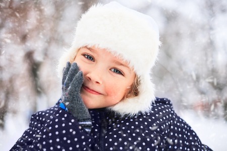 Portrait of a cute little girl in a snowy park during a snowfall.の写真素材