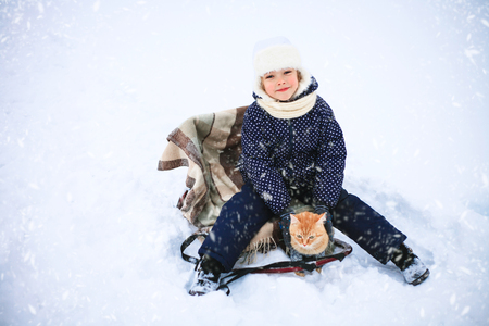 Little girl and a red cat on a sleigh ride in the countryside.の写真素材
