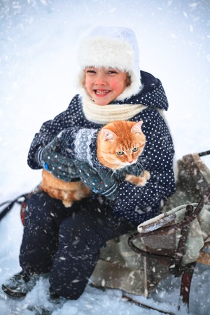 Little girl and a red cat on a sleigh ride in the countryside.の写真素材