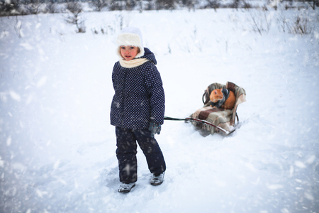 Little girl drove sleigh whith a red cat on snow in the countryside.の写真素材
