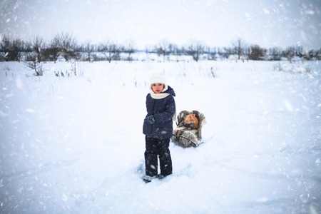 Little girl drove sleigh whith a red cat on snow in the countryside.の写真素材