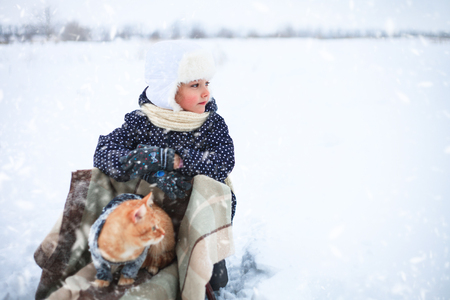 Little girl and a red cat on a sleigh ride in the countryside.の写真素材