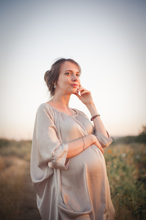 Portrait of a young beautiful pregnant woman on nature in the sunset light.の写真素材