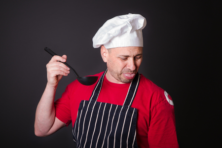 Portrait of a displeased cook with a ladle in his hand in the studio on a black backgroundの写真素材
