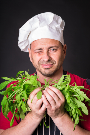 Closeup of happy chef holding arugula beam on black backgroundの写真素材
