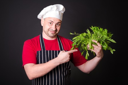 Closeup of happy chef holding arugula beam on black backgroundの写真素材