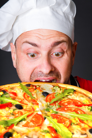 Portrait of happy attractive cook with a pizza in studio an a black backgroundの写真素材
