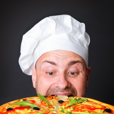 Portrait of happy attractive cook with a pizza in studio an a black backgroundの写真素材