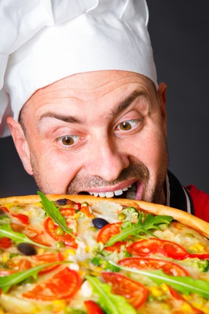 Portrait of happy attractive cook with a pizza in studio an a black backgroundの写真素材
