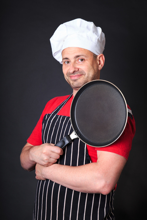 Studio shot of positive chef with a frying pan, over dark background.の写真素材
