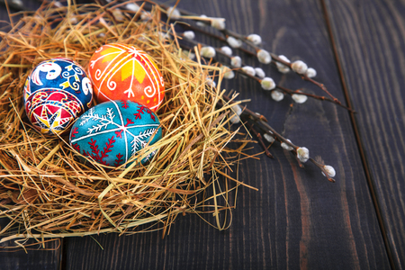 Easter eggs in a basket with willow twigs on a wooden table. The concept of the Easter holidays, and folk art.の写真素材