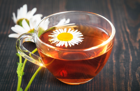 Chamomile tea in a transparent cup closeup, on a wooden table. The concept of herbal medicine.の写真素材