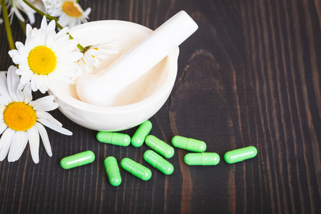 Chamomile flowers and green phytotherapeutic capsules on a wooden table. Herbal medicine and healthの写真素材