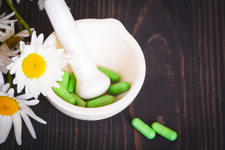 Chamomile flowers and green phytotherapeutic capsules on a wooden table. Herbal medicine and healthの写真素材