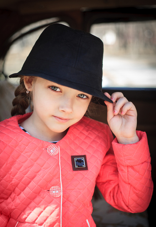 Portrait of a cute little girl with a black hat in a retro car.の写真素材